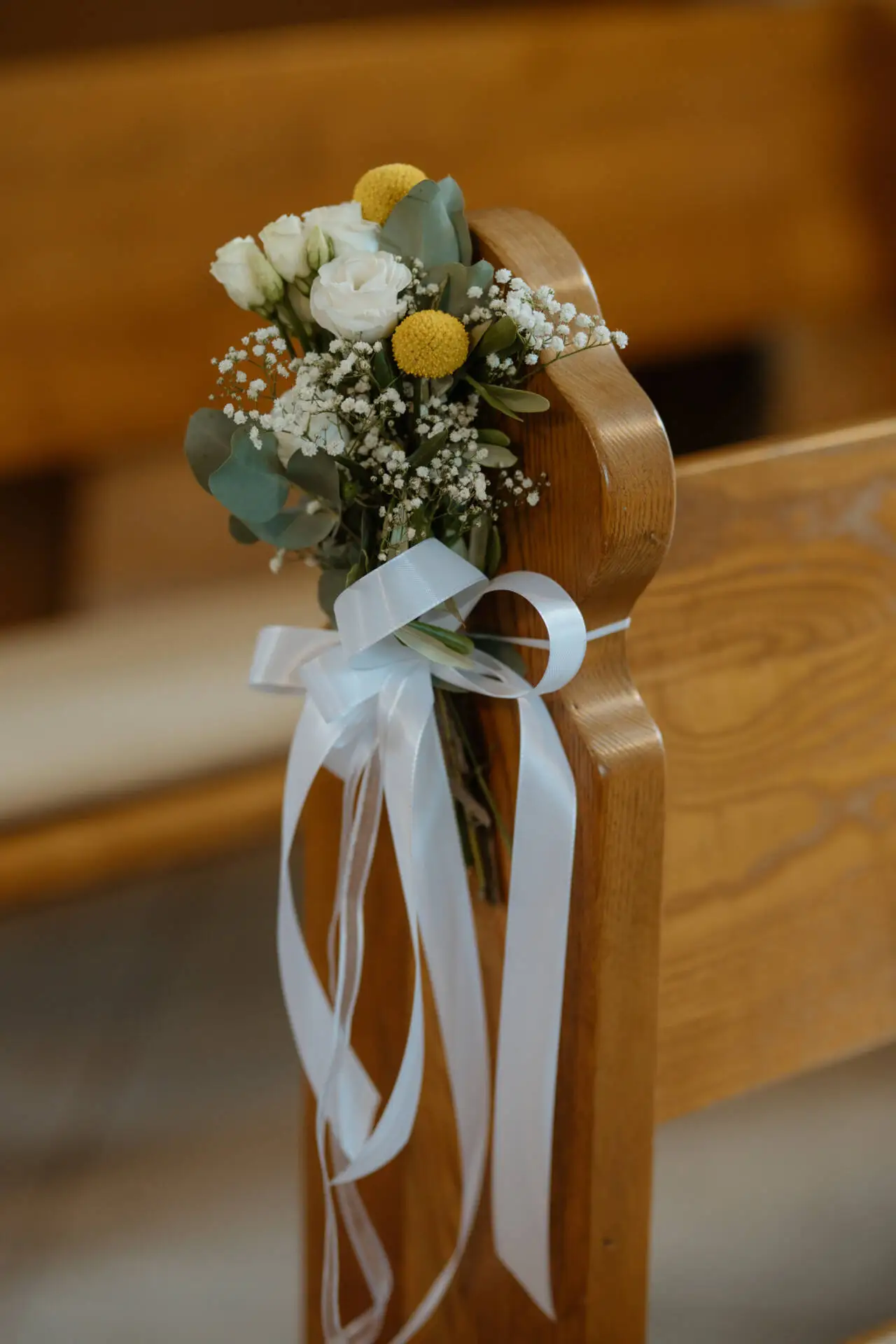 Blumengesteck mit weißen Schleifen auf Kirchenbank