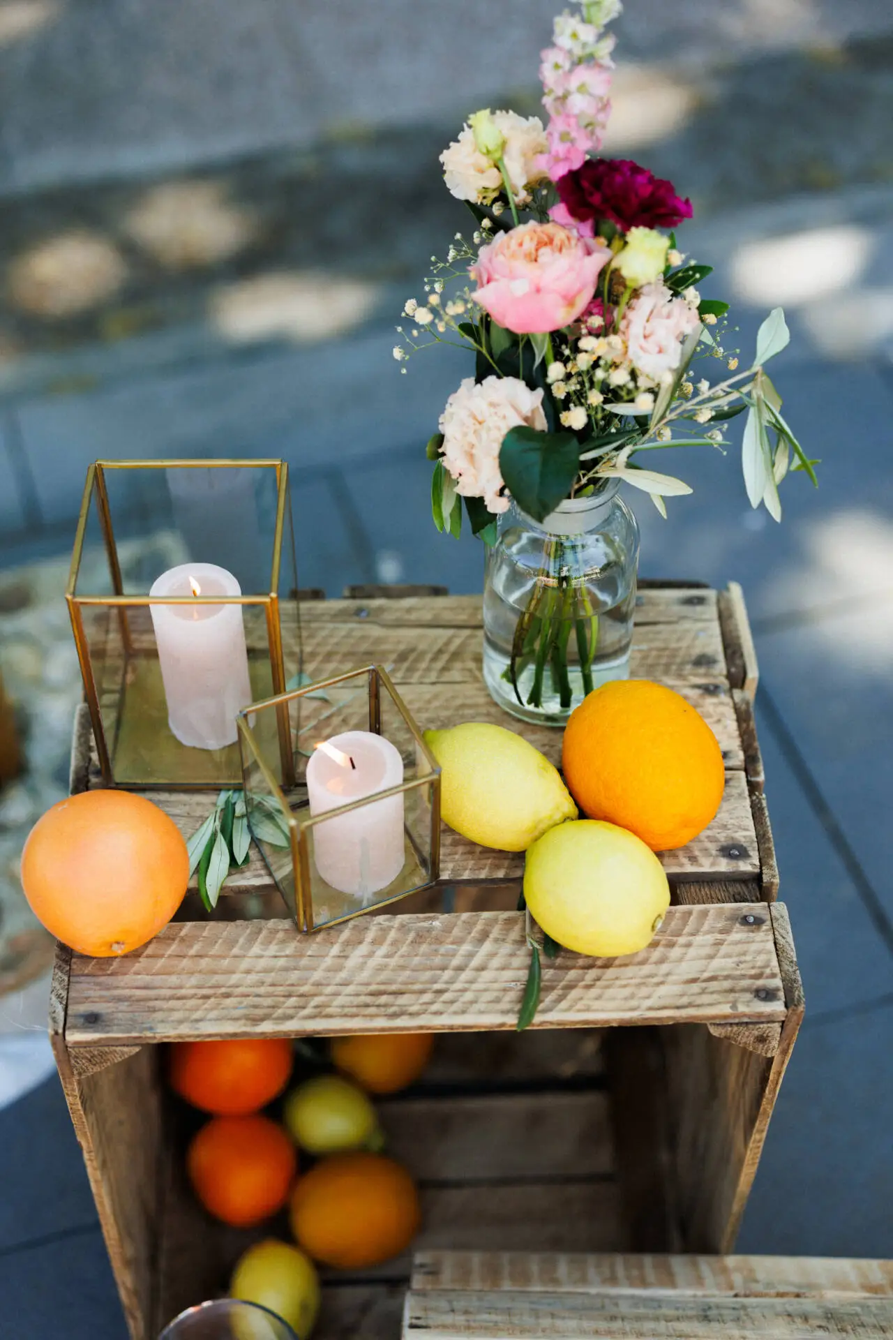 Blumen, Kerzen und Obst auf Holzkiste im Freien