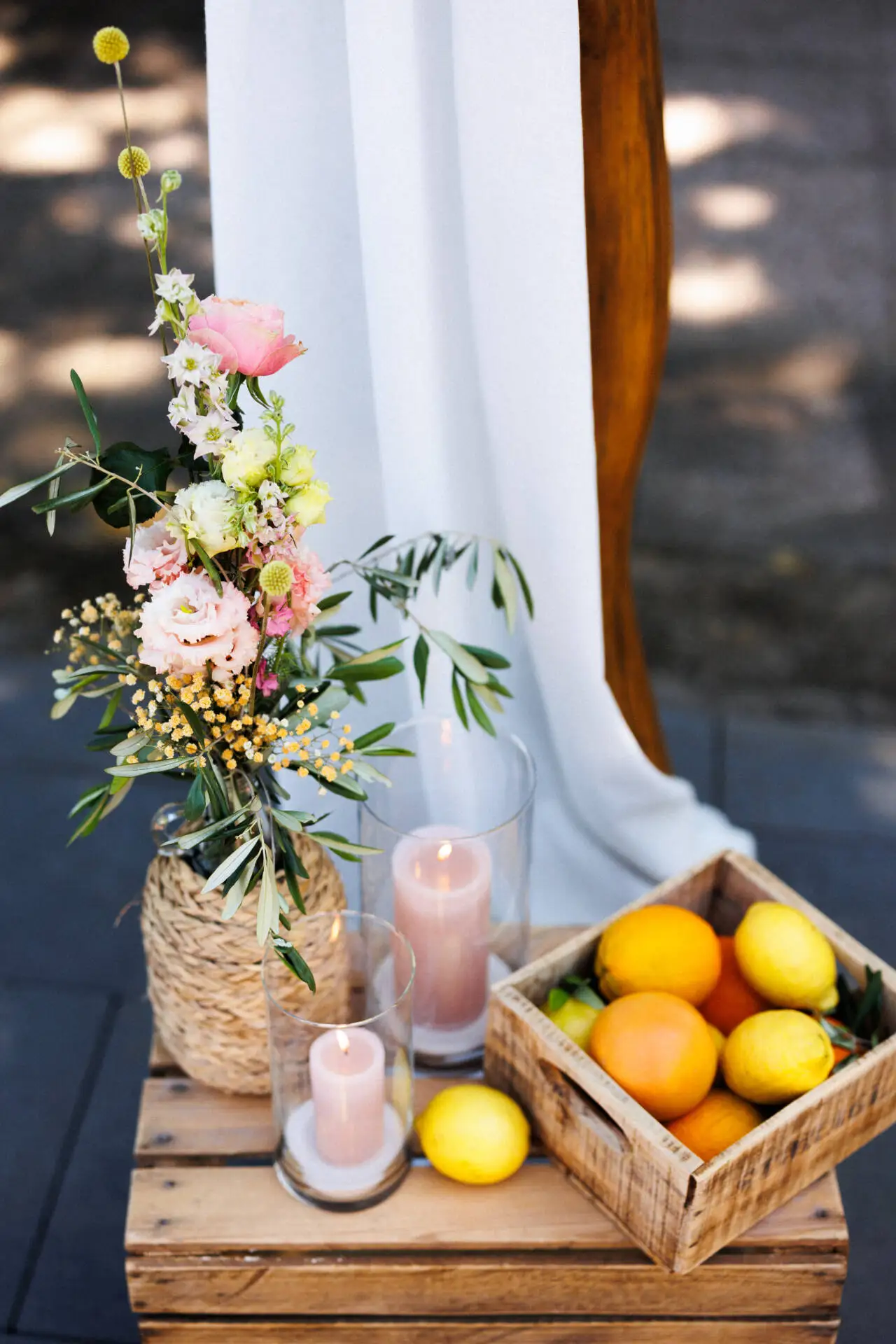 Blumenarrangement mit Kerze und Früchten auf Holztisch.