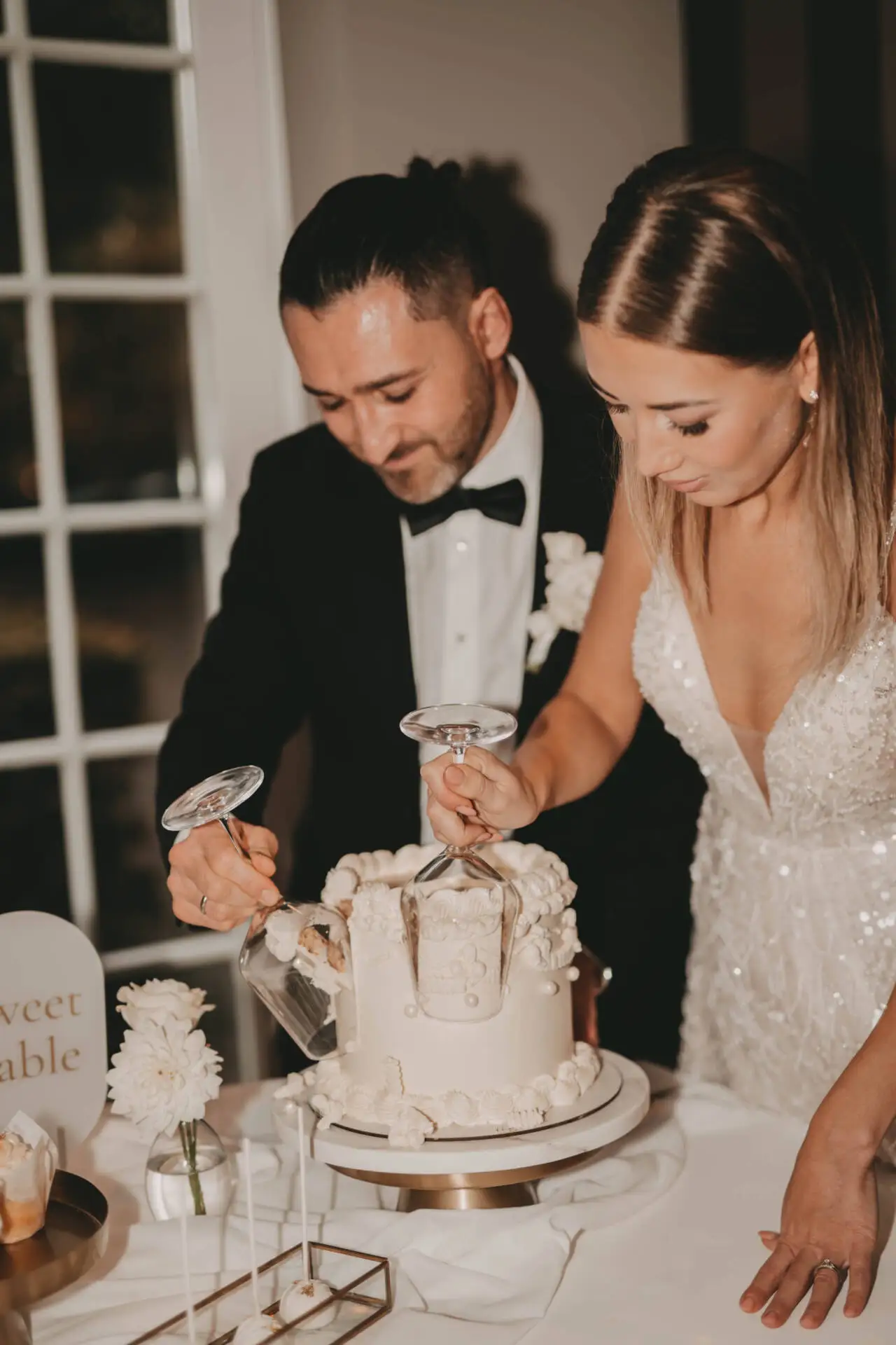 Brautpaar schneidet Hochzeitstorte mit Weingläsern an.