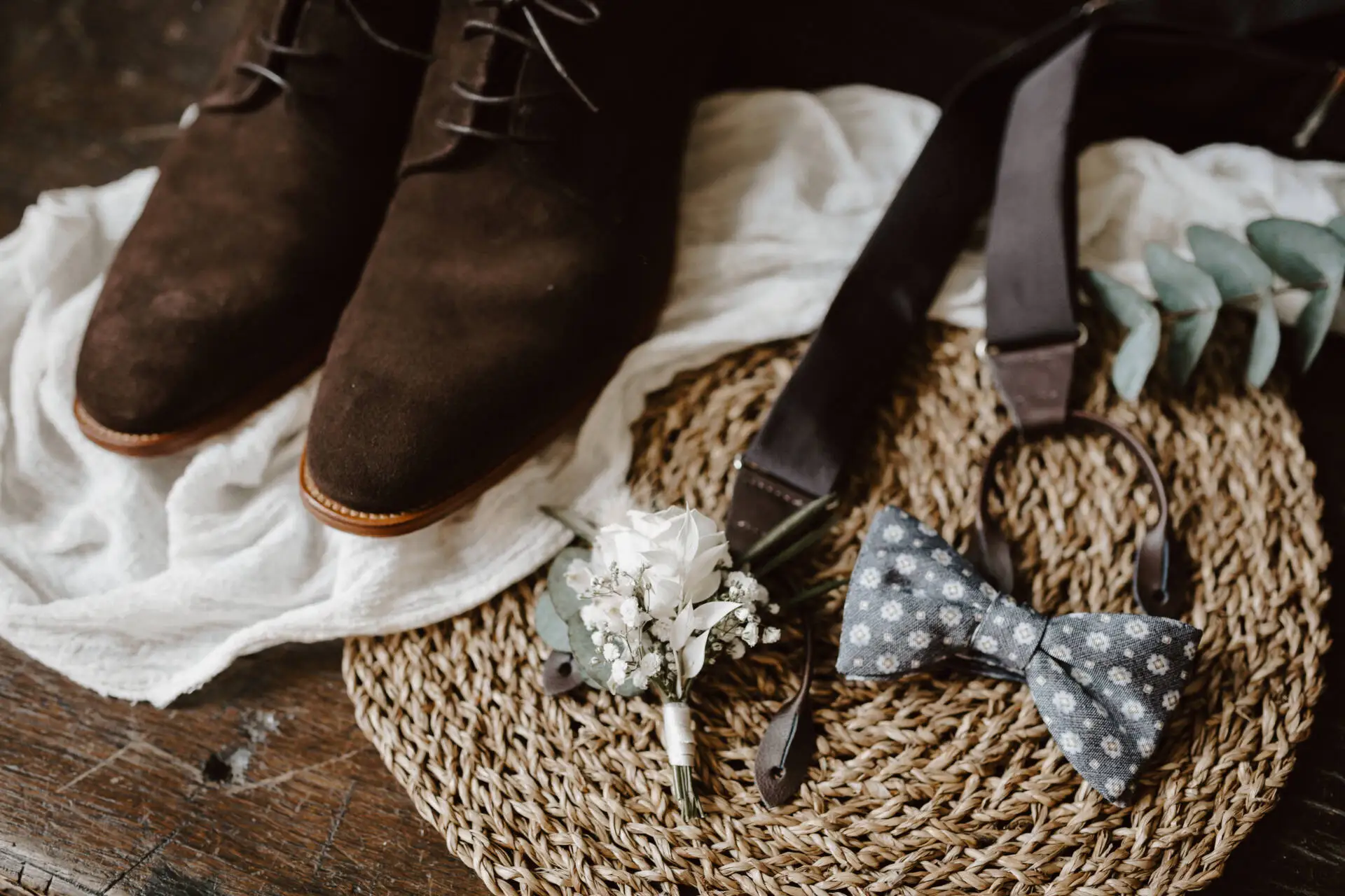 Braune Schuhe, Fliege und Blumenarrangement auf Tisch